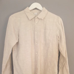 Beige skjorta i linne. - Säljer en stilren beige skjorta från Lindex i storlek EUR 158. Skjortan har långa ärmar och en klassisk krage med knappar framtill. Perfekt för en avslappnad men ändå uppklädd look.