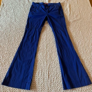 Blå/lila flare byxor - Snygga blå/lila byxor med utsvängda ben och låg midja. Byxorna har en klassisk design med knappar och dragkedja framtill. Sitter väldigt fint på och mycket bekväma. Mer bilder kan skickas vid intresse. 