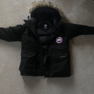 Svart dunjacka från Canada Goose - Säljer en svart dunjacka från Canada Goose med pälskantad huva. Jackan har en klassisk design med dragkedja och flera praktiska fickor. Perfekt för att preppa inför nästa års kalla vinterdagar. Det ända slitaget som finns på jackan är dragkedjan, stygnen som håller fast den på jackan har gått sönder men det går fortfarande att använda dragkedjan (Kan skicka bilder). Var absolut inte rädda för att buda💯
