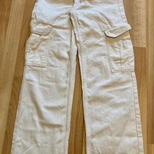 Vita cargobyxor från H&M - Säljer ett par vita cargobyxor från H&M med justerbar och låg midja. Byxorna har stora fickor på sidorna och är i mycket bra skick, har inte använt de mycket alls.💕💕💕