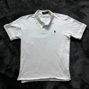 Ralph Lauren pike - Säljer en klassisk vit pikétröja från Ralph Lauren med broderad logga på bröstet. Tröjan har korta ärmar och en stilren krage med knappar. Perfekt för en avslappnad men ändå stilfull look. Storlek L, skick 10/10. Pris går att diskutera✅