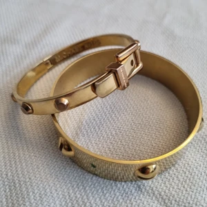 Guldarmband med nitar - Michael Kors - Två stilrena guldarmband med nitar från Michael Kors (äkta) Det ena armbandet har en smalare design med små nitar, medan det andra är bredare med större nitar. Passar en xs eller s. 