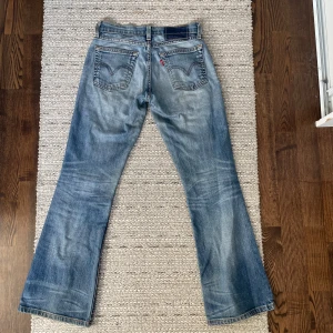 Blå bootcut jeans från Levi's - Snygga blå bootcut jeans från Levi's med klassisk femficksdesign och en liten röd etikett på bakfickan. Jeansen har en lätt tvättad look. De har en lågmidjad passform och är tillverkade i jeansmaterial. Köparen betalar frakten💕