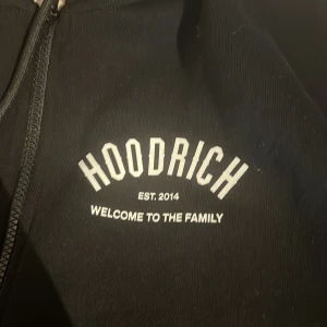 Svart hoodie från Hoodrich storlek S helt ny inte använd - Säljer en svart hoodie från Hoodrich med texten 'Welcome to the family' och 'Est. 2014' tryckt på både fram- och baksidan. Perfekt för en casual look med dragkedja framtill och en bekväm passform.