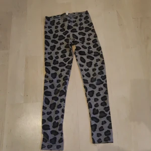Grå leggings med leopardmönster - Snygga grå leggings från H&M med ett coolt leopardmönster. Perfekta för en avslappnad stil med en touch av vildhet. De är stretchiga och bekväma, vilket gör dem idealiska för vardagsbruk.