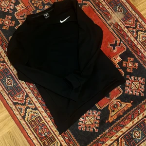 Svart tröja från Nike - Säljer en svart tröja från Nike med Dri-FIT teknologi. Tröjan har en enkel design med en vit Nike-logga på bröstet. Perfekt för träning eller vardagsbruk.