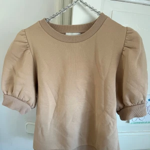 Fin brun/beige tröja från neo noir  - Säljer en söt brun/beige tröja från Neo Noir med puffiga korta ärmar och ribbad halsringning. 🤎