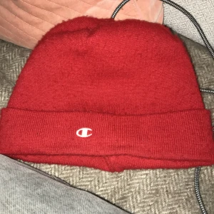 Röd mössa från Champion - Snygg röd mössa från Champion med det klassiska logotypen broderad framtill. Tillverkad i ett mjukt och bekvämt material som passar perfekt för kyligare dagar. Mössan har en uppvikt kant för extra stil och värme.