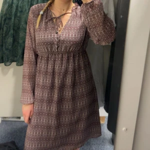 Mönstrad klänning från H&M Mama - Säljer en mönstrad klänning från H&M Mama i vinröd nyans. Klänningen har långa ärmar och en v-ringad hals med knytband. Perfekt för en bekväm och stilren look.