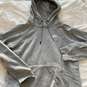 Grå hoodie från Nike - Säljer en klassisk grå hoodie från Nike med justerbar huva och känguruficka. Perfekt för en avslappnad stil. Den har långa ärmar och en liten Nike-logga på bröstet.