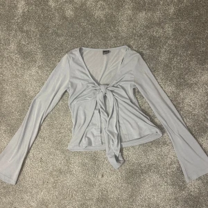 Ljusgrå knytblus från Gina Tricot - Säljer en stilren ljusgrå blus från Gina Tricot. Blusen har långa ärmar och en knytning framtill som ger en snygg detalj. Perfekt för att lägga till en touch av elegans i din garderob.