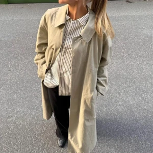 Beige trenchcoat - Säljer denna beige trenchcoat med en oversized passform och nedhasade axlar. Jackan har knappar framtill och en klassisk krage. Perfekt för en chic och avslappnad look. Köpt för 1000kr💕i nyskick med prislapp kvar!