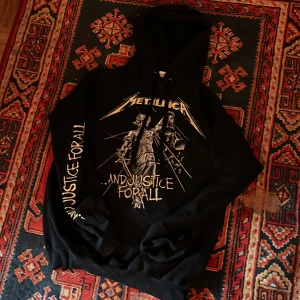 Svart Metallica hoodie - Säljer en svart hoodie med Metallica-tryck. Framsidan har ett stort tryck med texten '...And Justice For All' och bandets logga. Storlek M.