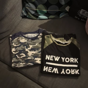 Två coola t-shirts med tryck & camo - Säljer två t-shirts i ungdomlig stil. Ena har blå och grön camouflage-mönster med mörkblå krage, den andra är svart med gröna camo-detaljer på axlarna och stort vitt 'NEW YORK' tryck fram. Perfekta för dig som gillar streetwear och statement-plagg.