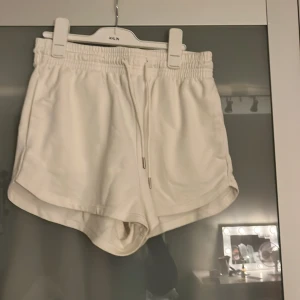 Vita mjuka shorts med snörning M - Superfräscha vita shorts med elastisk midja och snörning framtill. De har en sportig vibe med rundade benkanter och är gjorda i mjukt material som känns skönt mot huden. Perfekta för chill dagar eller träning.