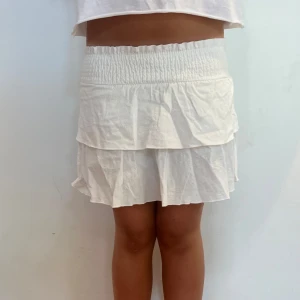 Vit volangkjol med resårmidja - Supersöt vit kortkjol med volanger och bred smockresår i midjan. 