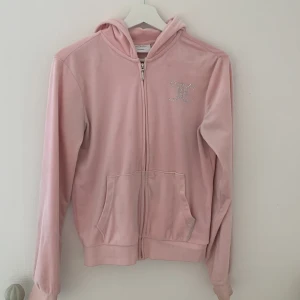 Rosa Juicy Couture velourjacka - Superfin rosa velourjacka från Juicy Couture med huva och glittrande strasstenar på bröstet och ryggen. Jackan har dragkedja och två fickor där fram. Perfekt för en chill och trendig look. Pris kan diskuteras !