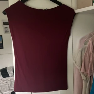 Vinröd tight tröja från 157 XS - Säljer en vinröd, tight och ärmlös tröja från 157 i storlek XS. Tröjan har enkel, rak design med rund halsringning och är tillverkad i ett stretchigt material som sitter snyggt mot kroppen.