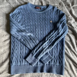 Blå kabelstickad tröja Morris - Kabelstickad blå tröja från Morris med rund halsringning och broderat märke bröstet. Tröjan har långa ärmar och ribbade muddar vid ärmslut och nederkant. Perfekt för dig som gillar klassisk och stilren look. Storlek S sitter som S. Ser lite använd ut men annars väldigt bra skick, och har fortfarande mycket kvar att ge! Mitt pris 299:- nypris 1699:-