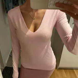 Ljusrosa långärmad v-ringad topp - Säljer en ljusrosa långärmad topp med v-ringning. Sitter tight och har en enkel, stilren design. Perfekt för dig som gillar en feminin och clean look. Materialet känns mjukt och stretchigt, troligtvis bomull eller polyester.