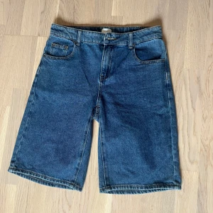 Blå jeansshorts från Grunt - Klassiska blå jeansshorts från Grunt med normal passform och raka ben. Shortsen har fem fickor, bälteshällor och stängs med knapp och dragkedja. 