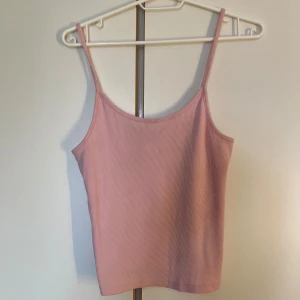 Ljusrosa ribbad linnetopp - Supersöt ljusrosa linnetopp med smala axelband och ribbad struktur. Toppen är ärmlös och har en enkel, rak passform som är perfekt till jeans eller kjol. Materialet känns mjukt och stretchigt, vilket gör den riktigt bekväm att bära. Lappen för storleken finns inte kvar men vet att det är storlek s