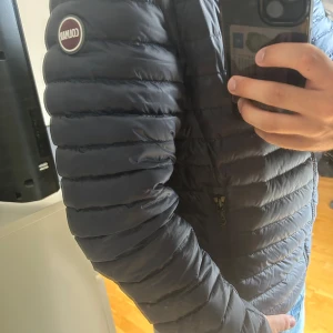 Blå dunjacka från Colmar - Snygg blå dunjacka från Colmar med quiltad design och dragkedja framtill. Jackan har hög krage, två sidofickor med dragkedja och Colmar-logga på ärmen. Perfekt för kyliga dagar och ger en clean, sportig look. Lite för liten i storleken men i princip ny. Nypris ligger på ca 2500, säljer för 600kr