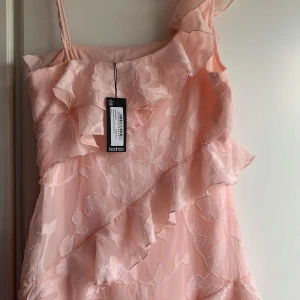 Rosa maxiklänning med volanger Boohoo - Helt ny klänning och inte använt ,PRIS KAN DISKUTERAS 🩷säljer pga att den inte passade  , den är i storlek 38 och en superfin ljusrosa maxiklänning från Boohoo med tunna axelband, asymmetrisk skärning och stora volanger💕💕. Klänningen har ett blommigt mönster i tyget och känns  romantisk och somrig. Det passar perfekt till bröllop , bal eller bara en sommarkväll 🩷