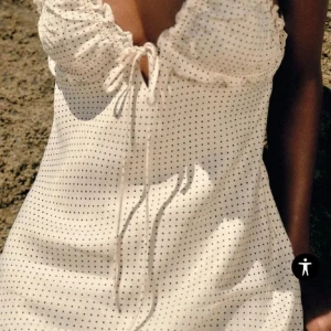 Vit lång prickig klänning med snörning - Superfin långklänning i vit med svarta prickar, tunna axelband och snörning framtill. Klänningen har öppen rygg och volangdetaljer vid bysten. Klänningen är några slitningar (se bilder) men skulle inte säga att det är något man tänker på. 