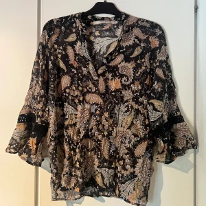 Mönstrad blus med volang  - Superluftig och skön blus med mönster och fint dekoration längs ärmarna. Passar allt från M-2XL