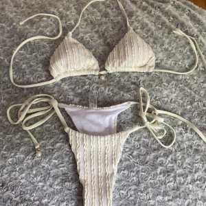 Vit bikini med pärldetaljer och volang - Supersöt vit bikini med volangiga ränder och pärldetaljer på snörena. Triangeltopp med knyt. Materialet är syntet. Aldrig andvänd. Storlek XS