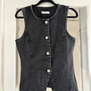 Svart jeanstopp - Snygg svart jeanstopp från Gina tricot med markerade sömmar och silverfärgade knappar framtill. Västen är ärmlös, har rund halsringning och en figurnära passform.