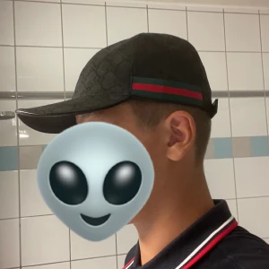 Svart Gucci keps äkta - Snygg svart keps från Gucci med klassisk röd och grön rand på sidan. Kepsen har böjd skärm, justerbart spänne bak och diskret GG-mönster i tyget. Perfekt accessoar för att lyfta din outfit med en lyxig touch.                            Köpt för 2600 här på plick också!