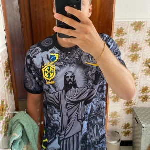Nike Brasil Dri-Fit fotbollströja S - Unik svart och grå Brasilien fotbollströja från Nike med Dri-Fit material. Framsidan har ett stort tryck av Kristusstatyn, detaljerade grafiska mönster och gula Brasil-loggor. Korta ärmar och rund hals. Perfekt för dig som vill sticka ut på planen.
