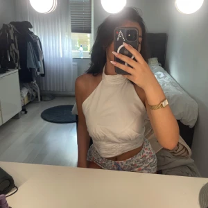 Topp - Säljer en vit omlott halterneck topp från Gina Tricot i storlek 36. Toppen är ärmlös med hög hals och knytning i ryggen, vilket ger en snygg och trendig look. Perfekt för varma dagar och enkel att styla med olika outfits.