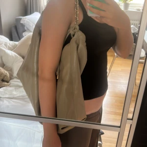 Beige axelväska i skinn från H&M - Säljer en stor och mjuk beige axelväska från H&M i skinnimitation. Väskan har en chunky guldfärgad kedja som axelrem och snygg snörning upptill. Perfekt för dig som vill ha plats med allt du behöver och ändå se trendig ut.