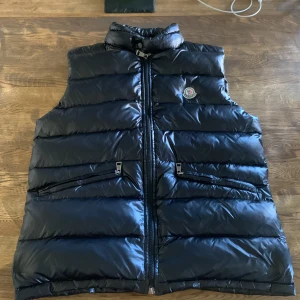 Svart moncler väst - Svart moncler väst,säljer för den inte används eller kommer användas.Jätte bra skick inga defekter,vet dock inte vilken storlek den är men den passar mig som har S och M och är 1,80 lång,skriv om mer bilder eller frågor