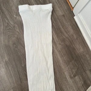 Vit ribbad långkjol - Säljer en vit långkjol med ribbad struktur. Kjolen är figurnära och har en enkel, stilren design som passar perfekt till sneakers eller boots. Materialet känns mjukt och stretchigt, vilket gör den bekväm att bära hela dagen.