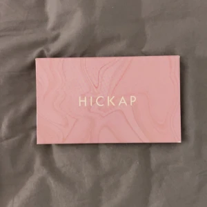 Hickap ögonskuggspalett med spegel - Säljer en snygg ögonskuggspalett från Hickap med 12 olika nyanser i både matta och skimriga toner. Färgerna går i beige, guld, orange, brunt, gult och grått. Paletten har en inbyggd spegel och kommer i en stilren rosa förpackning med marmormönster. Använt den mörkbruna en gång. 