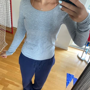 Ljusgrå långärmad tröja - En enkel och stilren ljusgrå långärmad tröja med rund halsringning. Tröjan har en slim passform och är tillverkad i ett mjukt och stretchigt material som känns skönt mot huden. Perfekt att matcha med jeans eller mjukisbyxor.