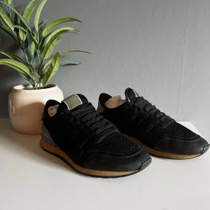 Valentino Rockrunner svarta sneakers - Snygga Valentino Rockrunner sneakers i svart med detaljer i vinrött och grått. Ovandel i mesh, mocka och skinn, med coola nitar på hälen och beige sula. Klassisk rund tå och snörning. Perfekta för dig som vill ha en lyxig streetstil. Dom har limmats en gång men helt fantastiskt bra bra sick skulle inte säga större skador än de är på bilderna passar storlek 44 också tveka inte med att skriva och fråga om mer bilder! Pris inte hugget i sten