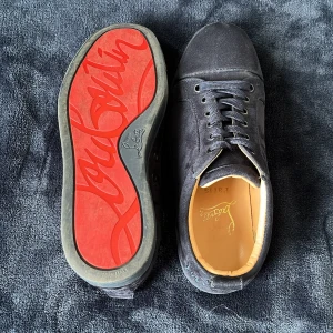 Mörkblå sneakers i mocka  från cristian Louboutin  - Snygga mörkblå sneakers från cristian Louboutin i mocka med klassisk röd sula och broderad logga på hälen. Perfekta för dig som vill sticka ut med exklusiva detaljer och lyxig känsla.