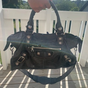 Svart Balenciaga City handväska i skinn - Ikonisk svart Balenciaga City handväska i mjukt skinn med silverfärgade detaljer, dragkedja framtill och dekorativa nitar. Väskan har både handtag och avtagbar axelrem för olika stilar. Dustbag finns samt spegel!!  Skriv för flera bilder 💖