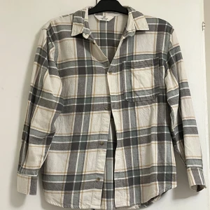 Rutig skjorta från H&M i bomull - Rutig skjorta från H&M i storlek 152. Skjortan har grå, beige och vita rutor, klassisk krage, bröstficka och knäppning framtill. Tillverkad i mjuk bomull och har långa ärmar. Perfekt för en chill och avslappnad stil. Pris kan diskuteras vid snabb affär
