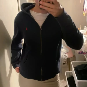 Mörkblå sipphoodie från Polo Ralph Lauren - Snygg mörkblå hoodie från Polo Ralph Lauren med dragkedja och huva. Klassisk röd logga broderad på bröstet och två fickor framtill💞Säljer pågrund av att armarna är för korta för mig!🫶🏻 tröjan passar för  XS/S🫶🏻💞  pris kan diskuteras!