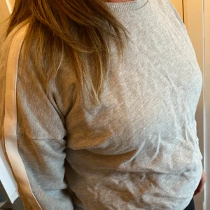 Grå sweatshirt med vit rand -  grå sweatshirt med rund hals och vita ränder längs ärmarna. 