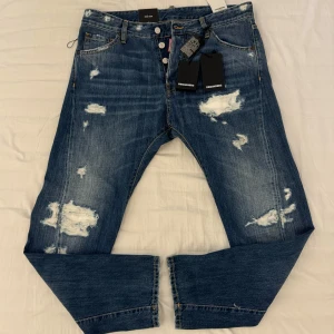Dsquared2 blå slitna jeans - ÄKTA, Riktigt snygga blå jeans från Dsquared2 med distressed detaljer och slitningar på flera ställen. Klassisk fickmodelm, raka ben och normal passform. Jeansen har knappar i gylfen och tydlig Dsquared2-logga vid fickan. Perfekta för en cool stil! LAPPARNA KVAR, ÄKTHETSBEVIS PÅ, SAMT HELT OANVÄNDA!!