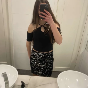 Svart offshoulder topp från H&M - Svart croppad topp från H&M med offshoulder och smala axelband som korsas framtill. Som bara vart använd ungefär 4 gånger. Toppen har en liten cut-out vid halsen och är ribbad i materialet. Perfekt för dig som gillar trendiga detaljer och en stilren look.