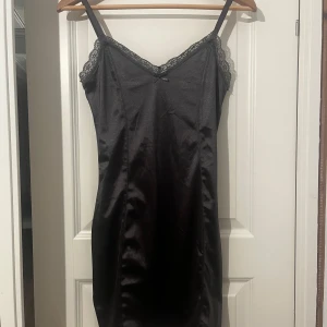 Grå satin klänning med spets - Supersnygg svart slipklänning i satin med tunna axelband och spetsdetaljer längs urringningen. Klänningen har en figurnära passform. Aldrig använd endast testad