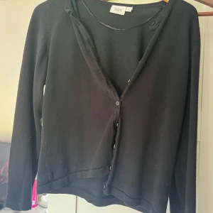 Svart kofta från Saint Tropez - En klassisk svart kofta från Saint Tropez i storlek S. Koftan har långa ärmar, rund halsringning och knäppning framtill med flera knappar. Perfekt att slänga över en topp för en enkel och stilren look.